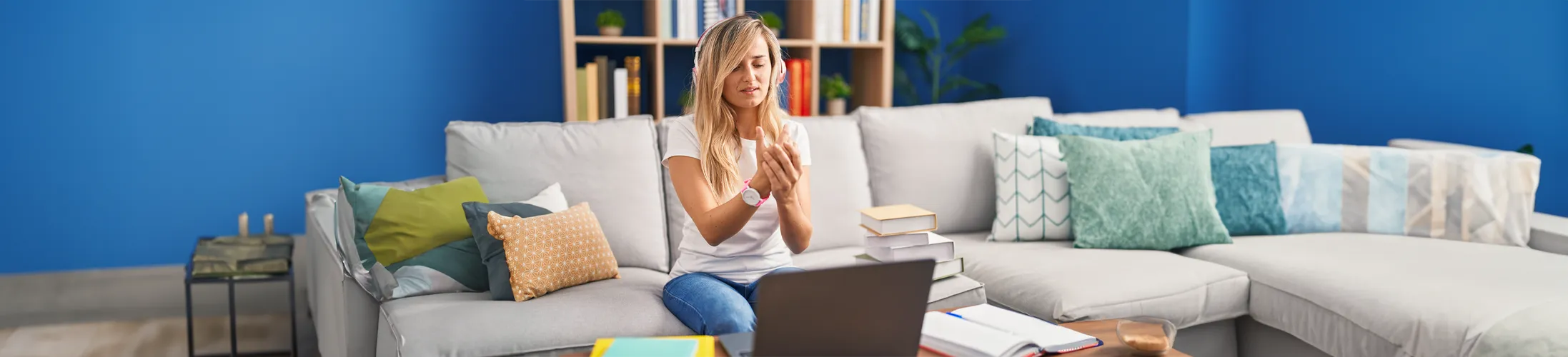 Arthrose im Handgelenk, Frau sitzt vor Laptop und hält sich die Hand, dumpfe Schmerzen und Brennen, Ursache oft Überlastung