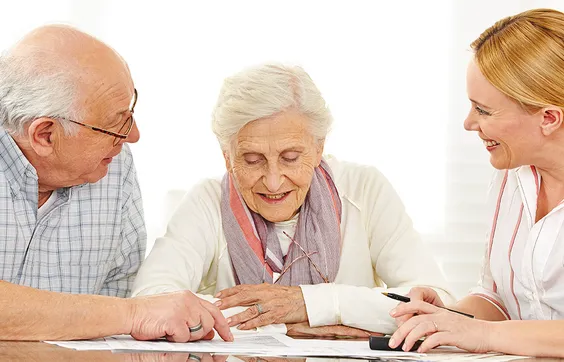 Parkinson, Hilfsmittelberatung im Sanitätshaus, ältere Dame vor Unterlagen mit Begleiter und Sanitätshausmitarbeiterin