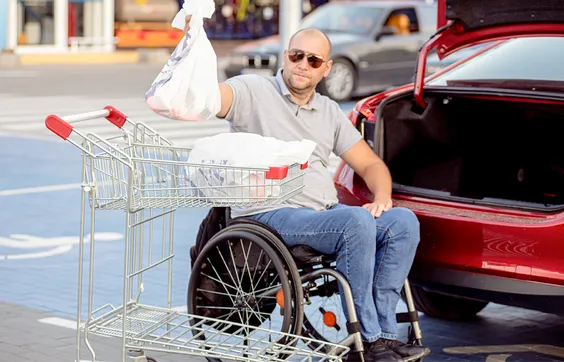 Parese, Mann im Rollstuhl legt Einkaufstüten in PKW-Kofferraum, Selbständigkeit, Mobilität