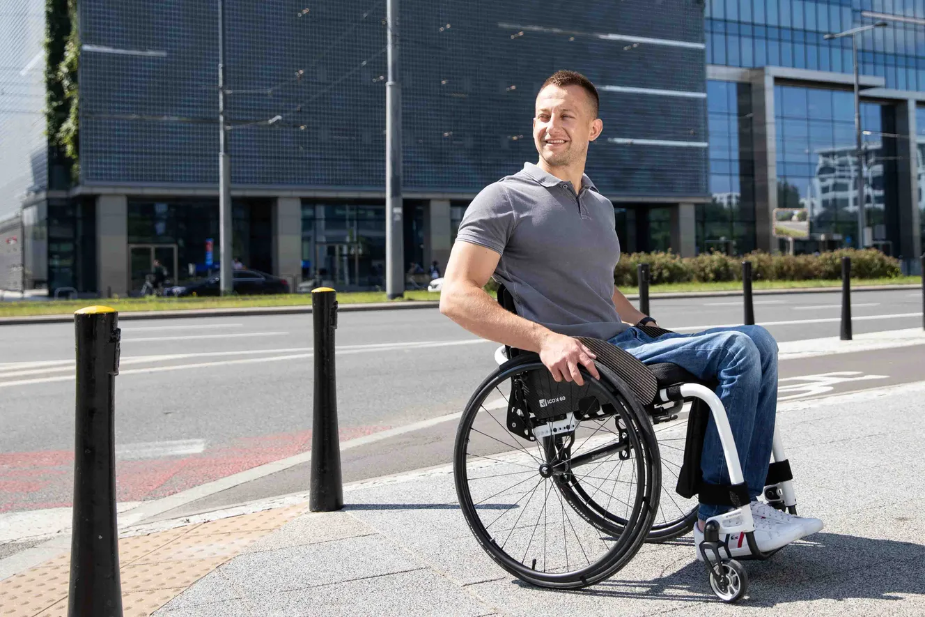 Mann sitzt in Icon-60 Rollstuhl von Rehasense, steht auf Straße, Gebäude im Hintergrund, Sonne scheint