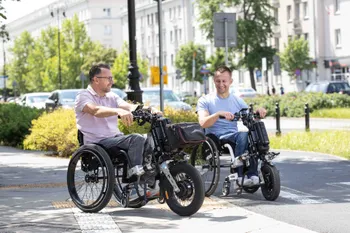 Zwei Männer sitzen in Rollstühlen mit Zuggeräten Paws von Rehasense, Vorderrad mit Lenker, Stadt, Straße