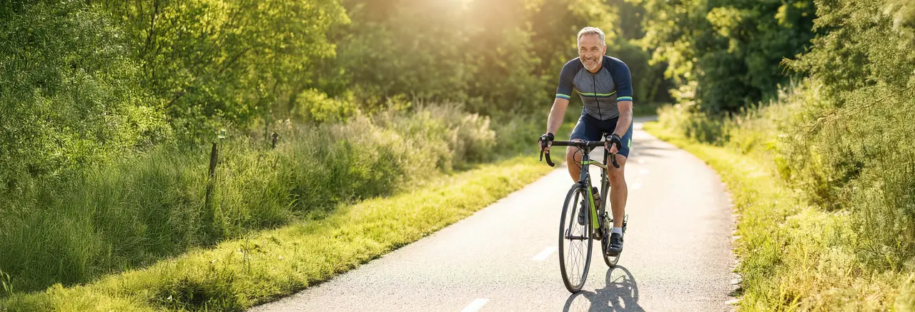 Älterer Radfahrer fährt lächelnd auf einem Rennrad durch eine grüne Landschaft