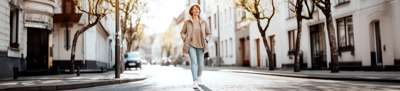 Frau mit Mischinkontinenz geht in der Stadt spazieren, Bäume und Häuser im Hintergrund