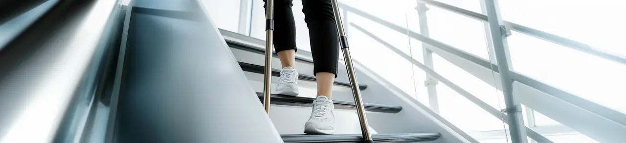 Person läuft mit Krücken die Treppe herunter, auf Bild sind nur die Beine und Füße zu sehen, Schattenwurf an der Wand im Hintergrund