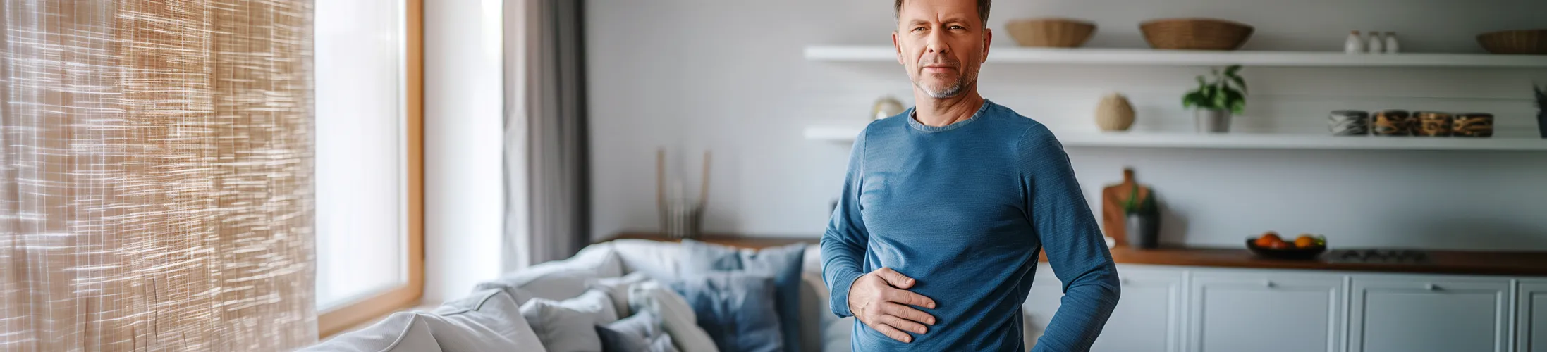 Stoma-Verstopfung lösen, Mann fasst sich zu Hause an den Bauch, Stoma-Blockade, sanftes Massieren der Stoma-Umgebung, mehr trinken