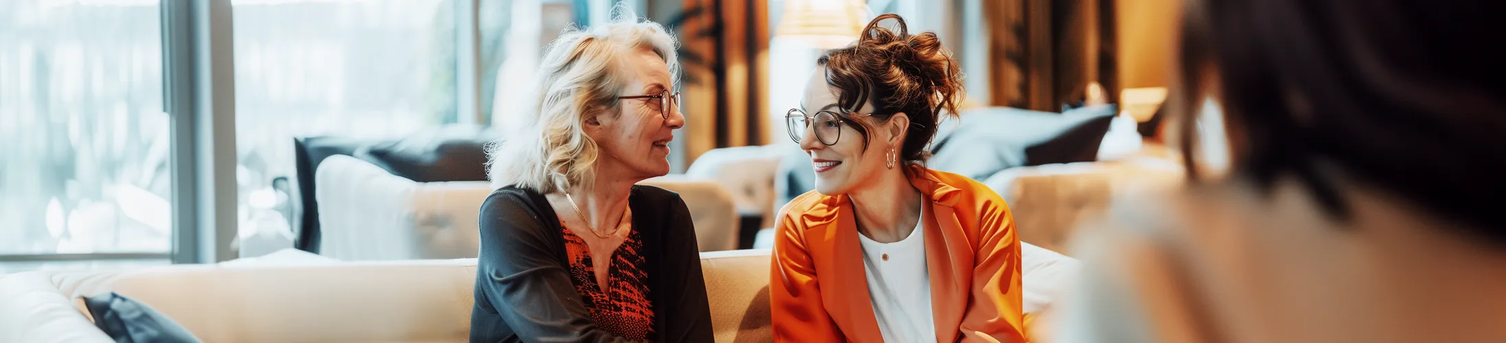 Nachtinkontinenz, zwei Frauen in den Wechseljahren sitzen auf Sofa und tauschen sich aus