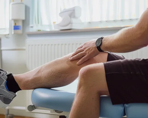 Meniskusriss-Behandlung, Mann sitzt auf Liege, eine Hand am Knie, Physiotherapie