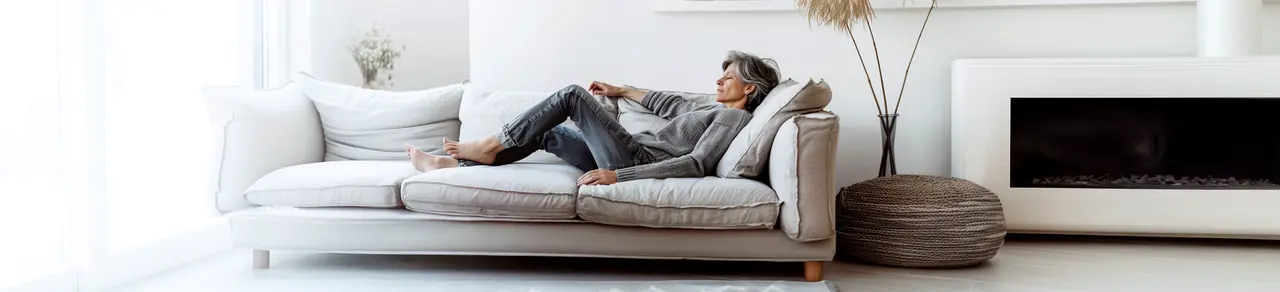 ältere Frau mit Krampfadern liegt auf Sofa im Wohnzimmer