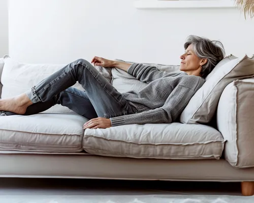 ältere Frau mit Krampfadern liegt auf Sofa im Wohnzimmer