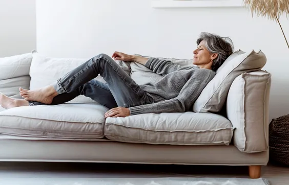 ältere Frau mit Krampfadern liegt auf Sofa im Wohnzimmer