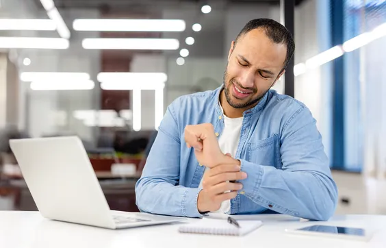 Karpaltunnelsyndrom, Mann an Laptop greift sich an schmerzendes Handgelenk