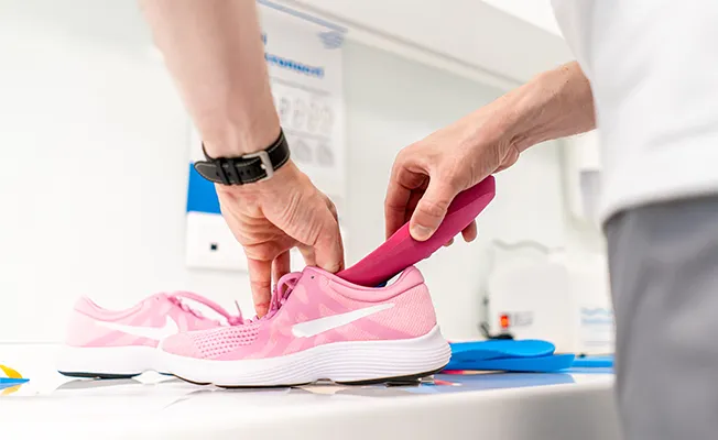 Fußschmerzen, Fachkraft in Sanitätshaus misst Sneaker aus, orthopädische Einlagen