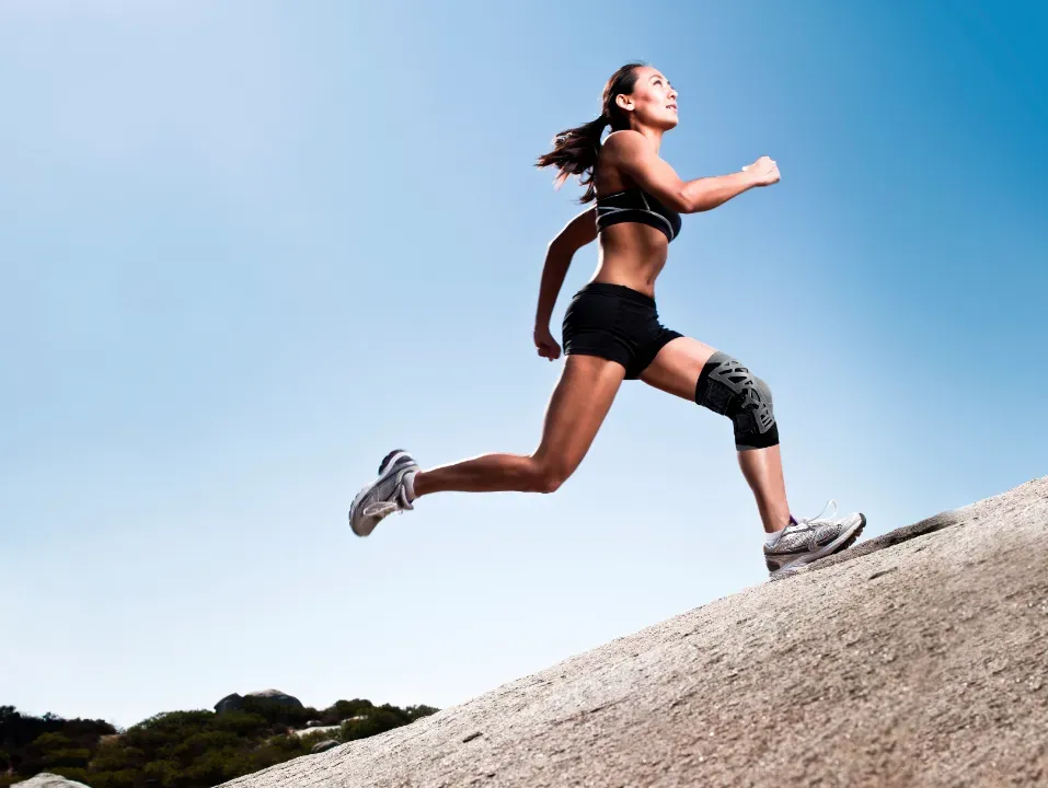 Frau mit Kniebandage und Sportkleidung läuft einen Berg hoch