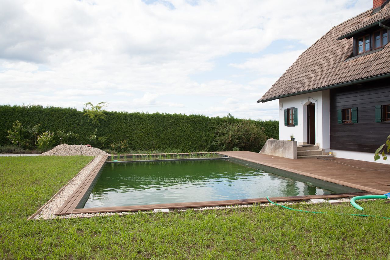 Naturpool im Garten mit Holzdeck und Kiesumrandung, ideal für den Bau eines Schwimmteichs oder Naturpools.