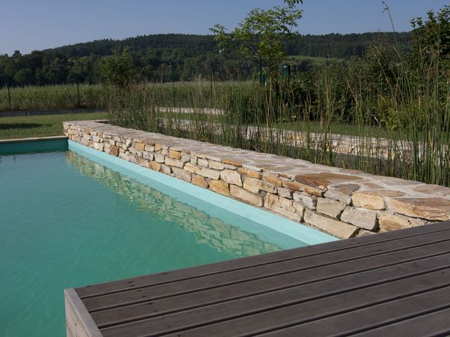 Ein rechteckiger Naturpool mit klarem, türkisfarbenem Wasser und einer Natursteinmauer an der Seite.