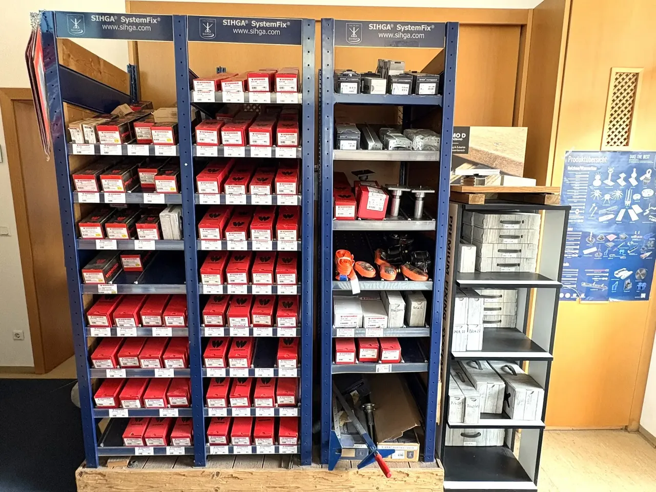 Mehrere Regale stehen im Holzhandel befüllt mit Holzbau Zubehör wie Holzbauschrauben und Edelstahlschrauben für Befestigung von Holzbauprodukten.