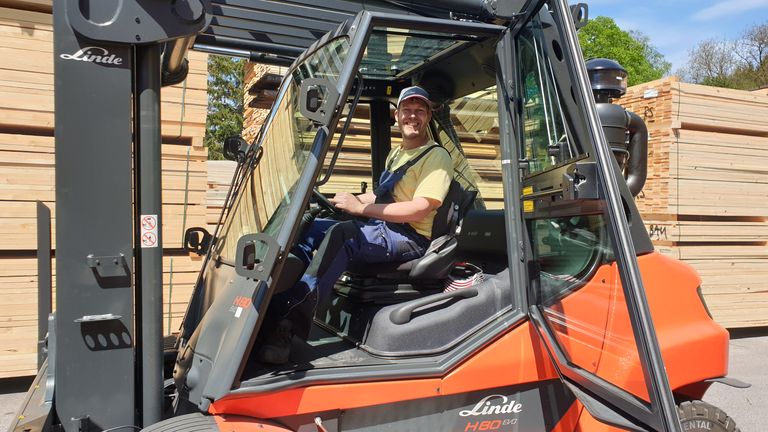 Lächender Mitarbeiter am Stapler während seiner Arbeit mit Holz