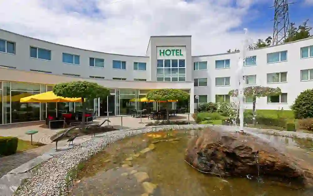 The photo shows a peaceful scene outside the Hotel Grauholz in Ittigen, with a rippling fountain creating a relaxing and welcome atmosphere in front of the modern building.