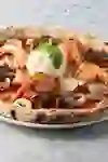Pizza aux fruits de mer cuite au feu de bois avec des crevettes, des escargots, des calamars, des clams et une boule de mozzarella surmontée de basilic, sur une surface en marbre.
