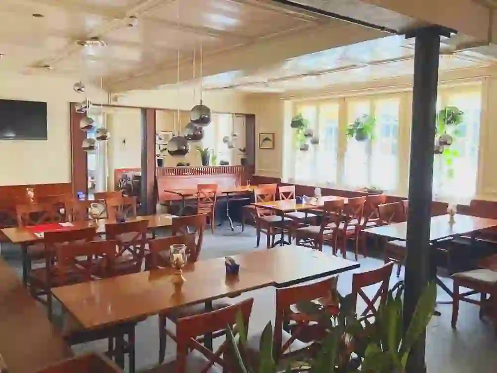 L'immagine mostra un salotto luminoso e invitante, con molta luce naturale che filtra dalle grandi finestre. I mobili in legno e i colori caldi creano un'atmosfera accogliente. Le piante appese e le lampade eleganti conferiscono all'ambiente un'atmosfera moderna e accogliente.