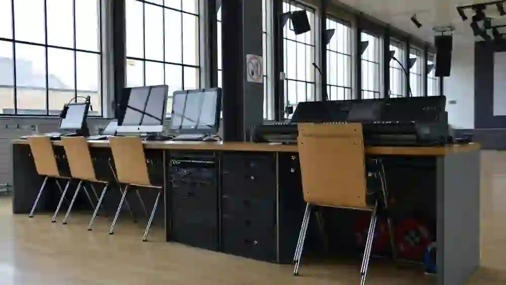 Un pupitre technique avec divers appareils et moniteurs dans un espace lumineux, préparé pour un événement ou une présentation.