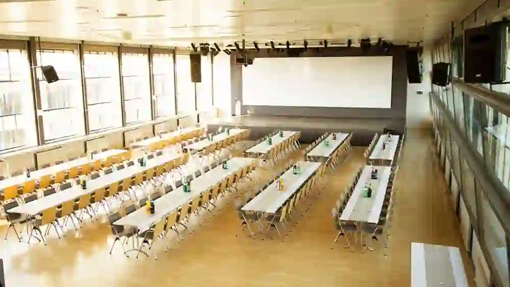 Une salle de séminaire lumineuse, inondée de soleil, avec des tables et des chaises bien rangées. L'atmosphère est calme et ordonnée, prête pour la formation et l'échange.