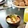 L'image montre un petit-déjeuner agréablement présenté dans un restaurant. Plusieurs crêpes dorées au four, légèrement saupoudrées de sucre glace, sont disposées sur une assiette blanche. À côté se trouve un petit pot de sirop d'érable. Un verre de jus d'orange et un set de couverts plié sur une serviette sont également visibles. En arrière-plan se trouve un vase avec des renoncules roses, et l'on peut également distinguer des salières et des poivrières. La scène est accueillante et appétissante, parfaite pour un petit-déjeuner ou un brunch décontracté.