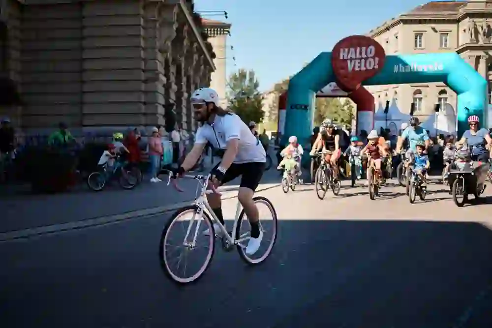 The photo shows a cycling event in which people of different age groups ride bicycles through an inflatable gate labelled "HELLO VELO!".