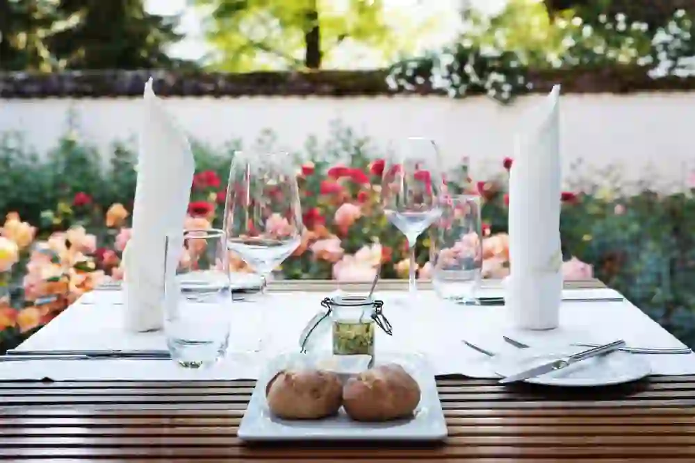 Une table soigneusement dressée en plein air par le restaurant Rosarium du château de Hünigen invite, devant un décor de roses en fleurs, à un repas idyllique qui promet le calme et le plaisir d'être ensemble.