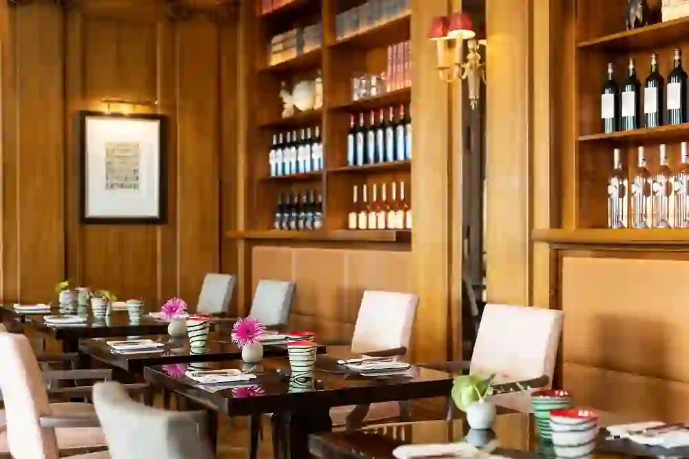 The picture shows the elegant Brasserie Vue in the Hotel Bellevue in Bern with wood-panelled walls, atmospheric lighting and carefully laid tables adorned with pink flowers, creating a warm and inviting atmosphere.