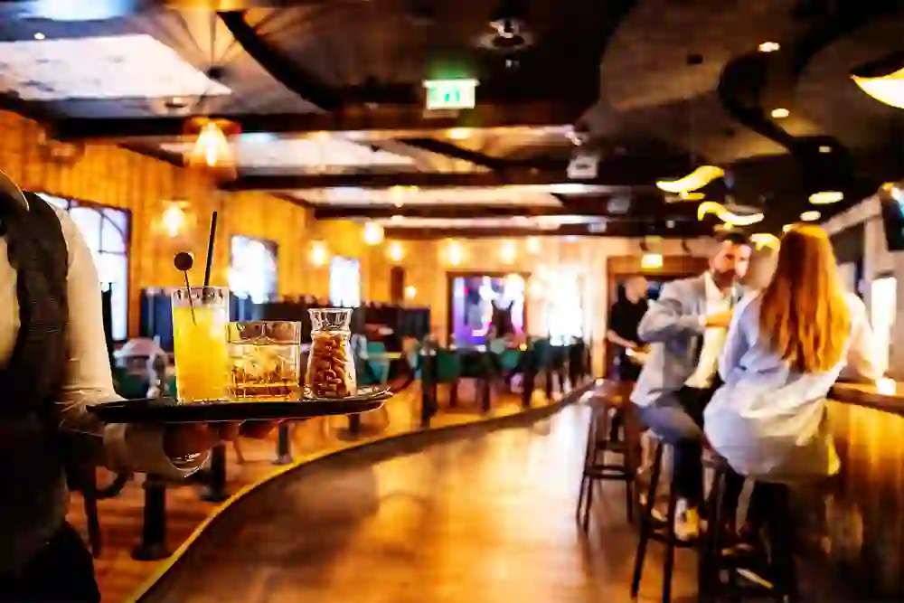 A bartender serves drinks in a warmly lit bar while guests chat in the background - the perfect atmosphere for relaxed evenings.