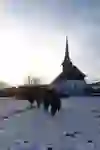 A group walks in the snow at dusk near a chapel, a moment of peaceful silence and fellowship during a guided night walk around Bern.