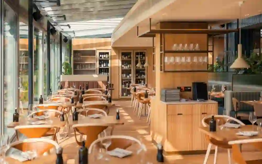 Auf dem Bild sieht man einen modernen Frühstückssaal. Grosse Fensterwände sorgen für eine helle, natürliche Beleuchtung. Die Tische sind gedeckt.