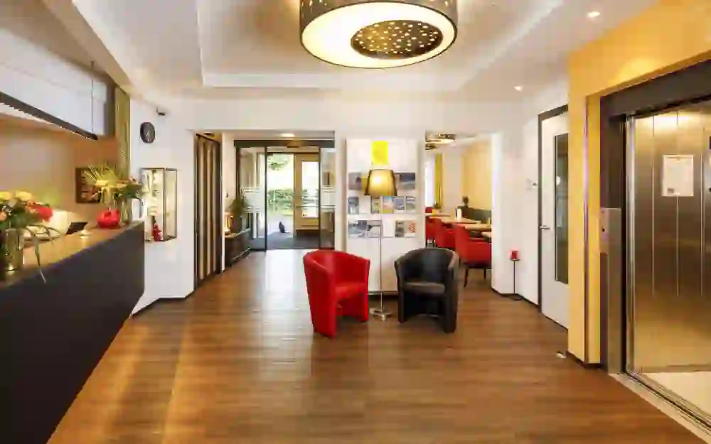 The picture shows the modern and inviting lobby of the Hotel Jardins with stylish red armchairs that convey an atmosphere of comfort and professionalism.