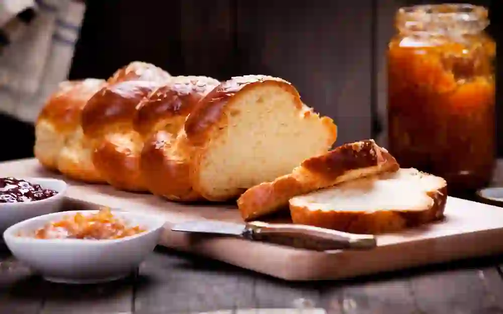 Das Bild zeigt eine appetitlich aussehenden Berner «Ankezüpfe», der auf einem Holzbrett serviert wird. Der Zopf ist goldbraun gebacken und zeigt die typischen glänzenden Oberfläche und die für einen Zopf charakteristische geflochtene Struktur.