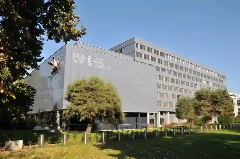 The picture shows the exterior view of the Universal Postal Union Congress Centre on a sunny day. The modern architecture with clear lines contrasts pleasantly with the surrounding greenery of the trees and radiates calm and professionalism.