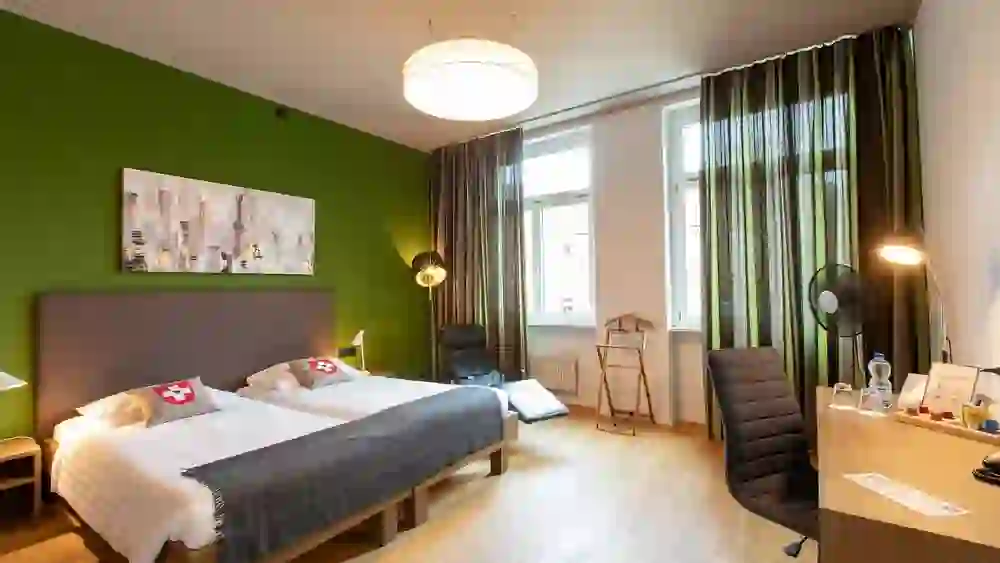 Das Bild zeigt ein helles und farbenfrohes Zimmer im Hotel Bären am Bundesplatz, das mit seiner frischen grünen Wand und gemütlichen Einrichtung eine lebendige und heitere Stimmung vermittelt.