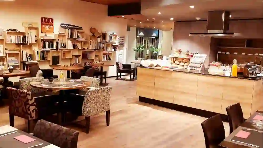 Das Bild zeigt den Frühstücksraum des Hotel Bären am Bundesplatz, der mit einem reichhaltigen Buffet und einer gemütlichen Leseecke zum Verweilen einlädt, was eine warme und einladende Atmosphäre schafft.