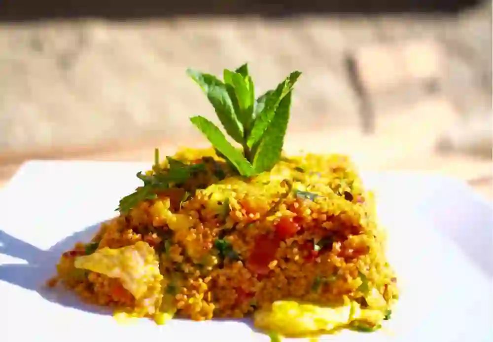 Ein kunstvoll angerichteter Teller mit leuchtendem, aromatischem Couscous, garniert mit frischer Minze. Das Gericht strahlt Wärme und Genuss aus, lädt zum Verweilen ein und vermittelt ein Gefühl von kulinarischer Freude und mediterraner Leichtigkeit.