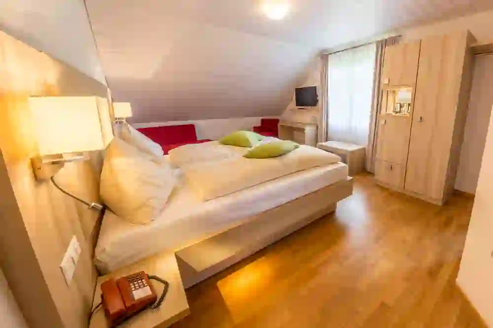 The picture shows a cosy, inviting bedroom in the Hirschen Eggiwil, with a large bed flanked by bedside tables and lamps. The red accents give the room a warm, comfortable atmosphere.