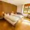 L'immagine mostra una camera da letto luminosa e accogliente con pareti in legno e un pavimento in parquet scintillante nell'Hirschen Eggiwil. Due letti con piumoni bianchi invitano a soffermarsi e la luce del sole che filtra dalla finestra crea un'atmosfera calda e accogliente.