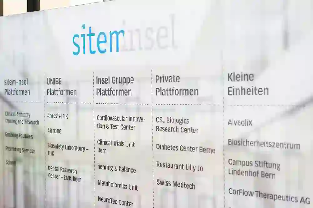 Auf dem Bild ist eine Glaswand mit dem Aufdruck „sitem-insel“ zu sehen, die verschiedene Plattformen und Einheiten listet, wie etwa für klinische Anatomie, kardiovaskuläre Innovation und private Plattformen.
