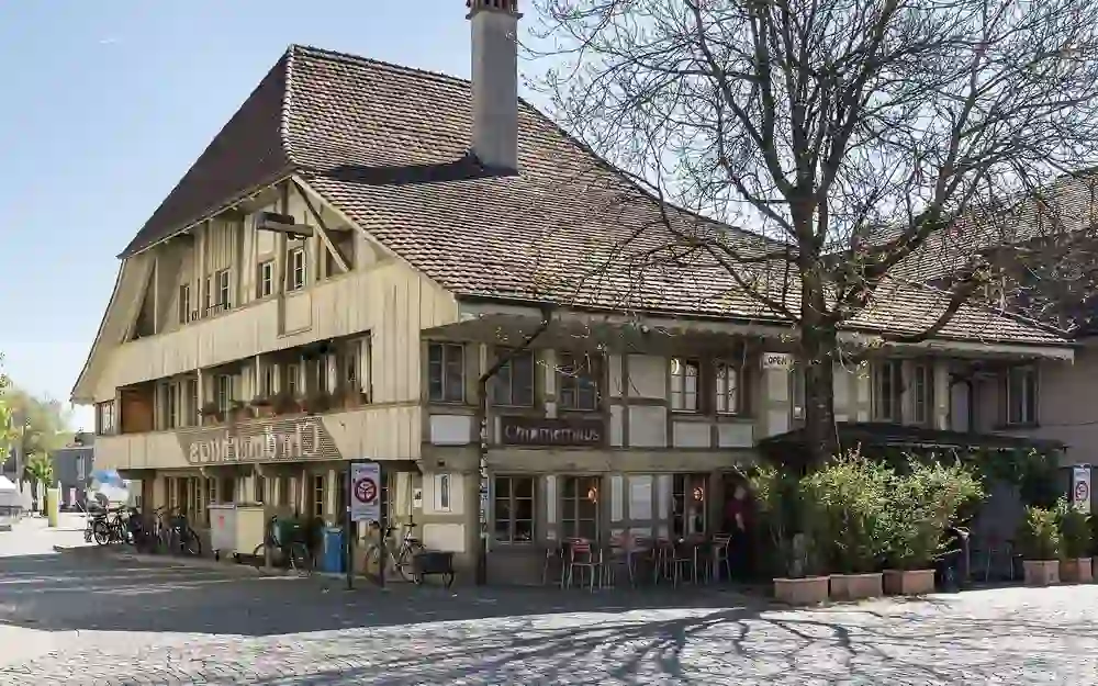 Das Bild zeigt ein traditionelles, charmantes Gasthaus mit Fachwerk und einer Außenterrasse in einer ruhigen Ecke. Die friedliche Stimmung wird durch das sonnige Wetter und die idyllische Umgebung verstärkt, die zum Verweilen einlädt.