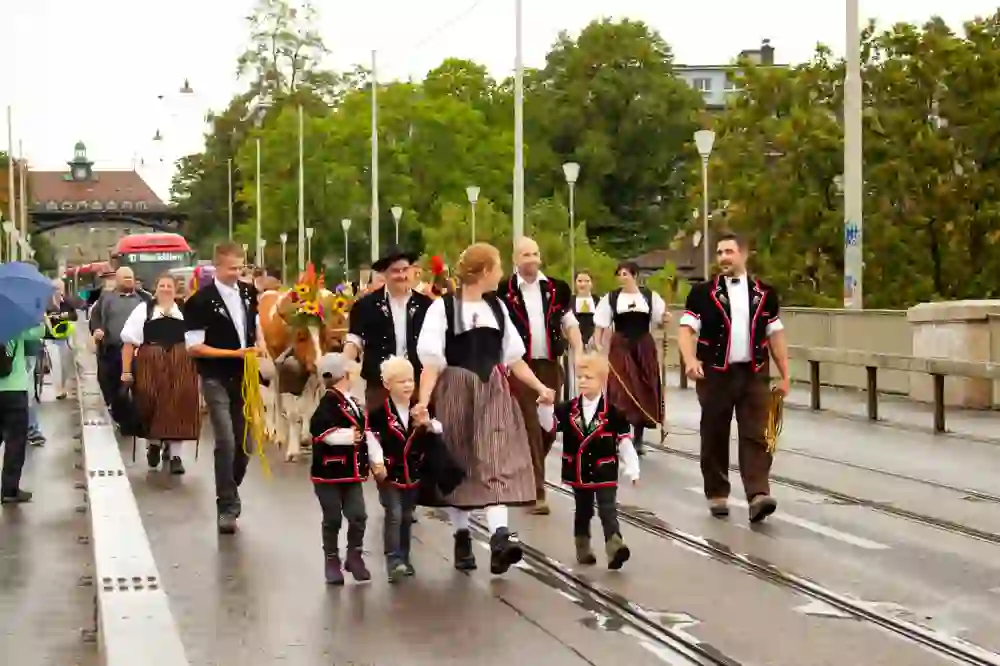 The picture shows the traditional Sichlete Alpabzug in Bern's old town. People in traditional costumes lead festively decorated cows through the streets. The cheerful atmosphere, despite the light rain, reflects the deep connection with tradition and community.