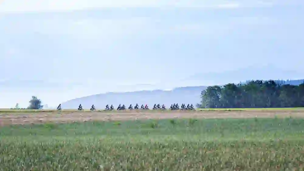 Eine Radlerkolonne zieht ihre Spur durch die friedliche Landschaft, ein stilles Panorama mit fernen Bergen, eingefangen in einem Moment gemeinsamer Harmonie.