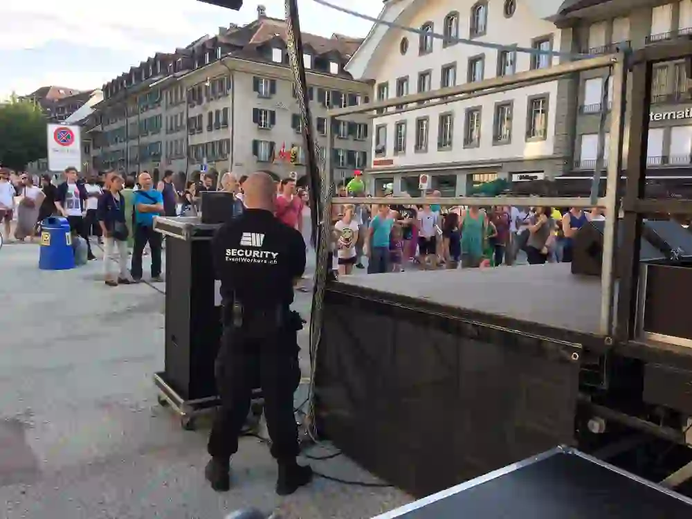 A security guard attentively holds the position behind the stage while the audience gathers in front of the stage - relaxed but vigilant.