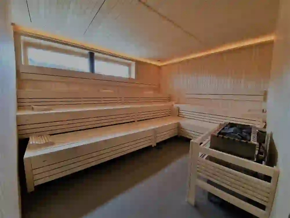 L'intérieur d'un sauna au bois clair et à l'éclairage apaisant, le poêle prêt pour la prochaine cérémonie d'infusion. Accueillant et vide, il promet chaleur et bien-être, un lieu de repos paisible.