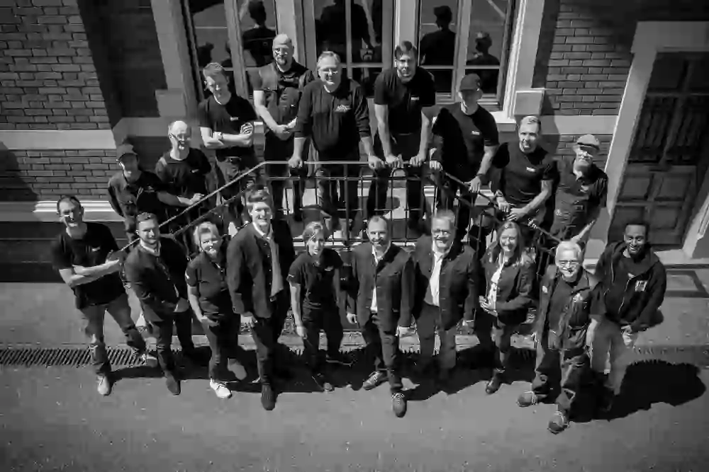 Un gruppo di persone sorridenti, presumibilmente il team del birrificio Felsenau, si trova insieme su una scalinata. La foto in bianco e nero irradia comunità e orgoglio.