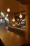 L'immagine mostra l'interno suggestivo di un'enoteca con un'illuminazione moderna, un lungo tavolo in legno e un'affettatrice di prosciutto in primo piano. I portabottiglie illuminati conferiscono all'ambiente un'atmosfera calda e invitante.