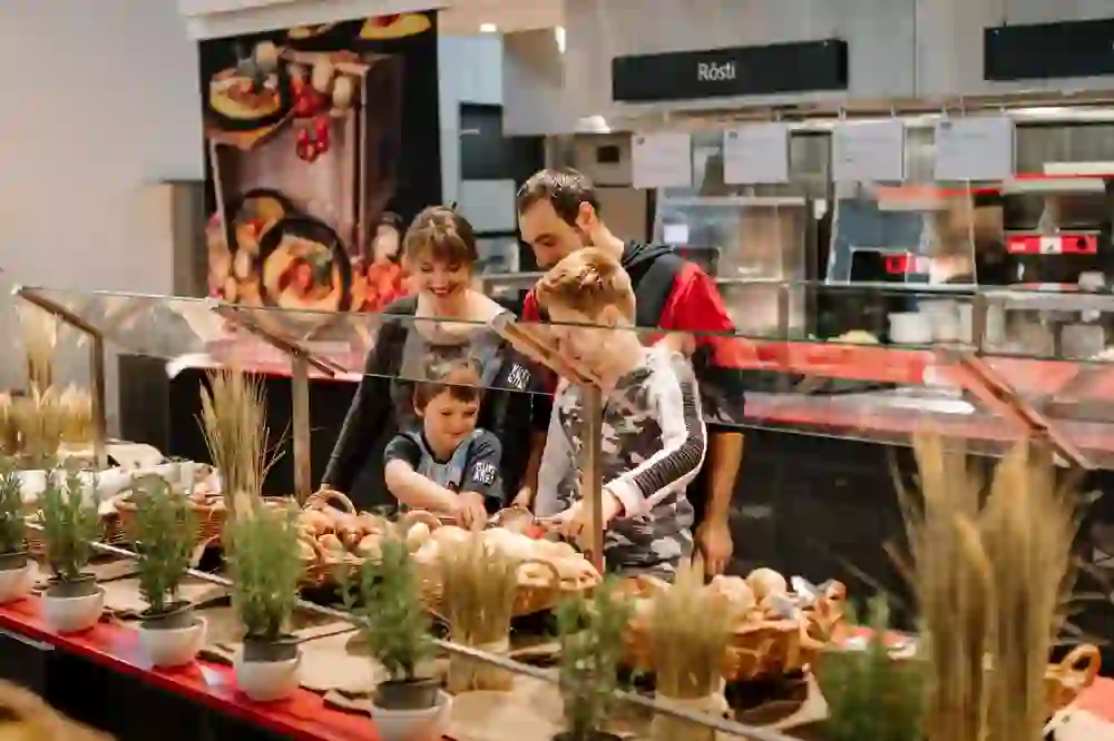L'ambiance familiale chaleureuse qui règne lors du choix des petits pains frais au buffet du brunch du Tapis Rouge sur le Gurten est palpable. Les visages souriants et l'anticipation commune d'un délicieux repas créent une image de sécurité et de plaisir.